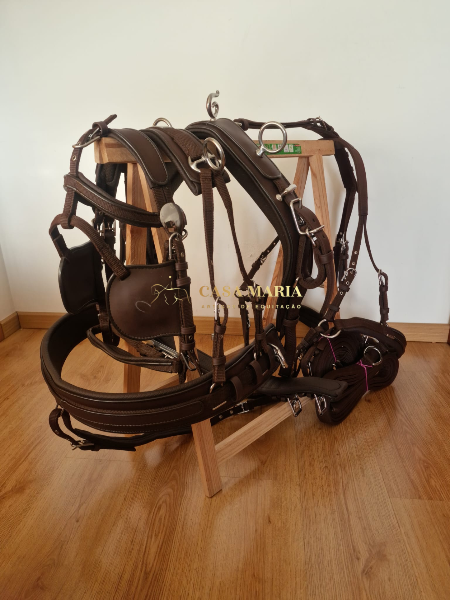 Arnês de equitação em couro castanho com fivelas metálicas prateadas sobre suporte de madeira