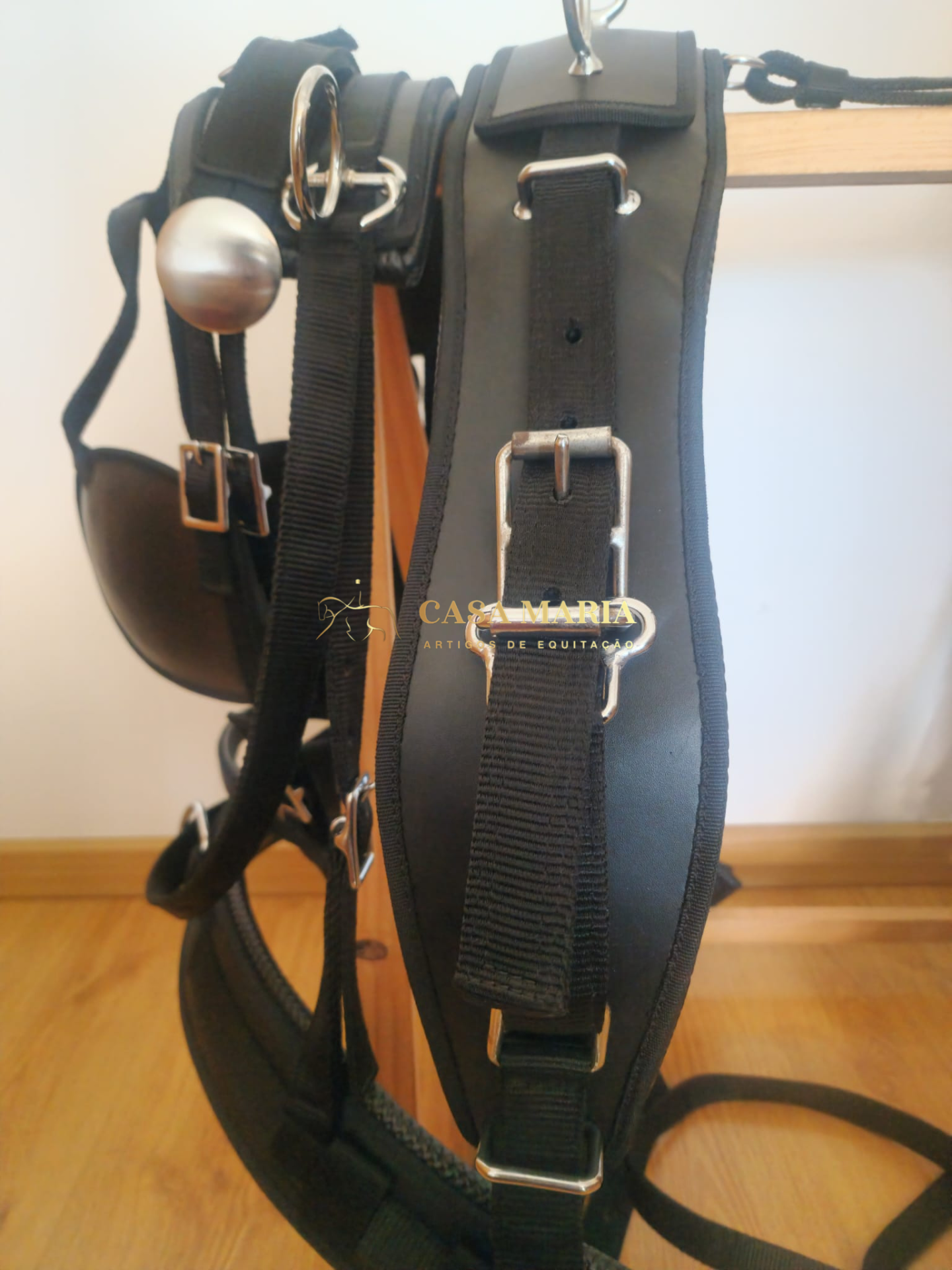 Arreio de equitação preto com fivelas metálicas pendurado em suporte de madeira
