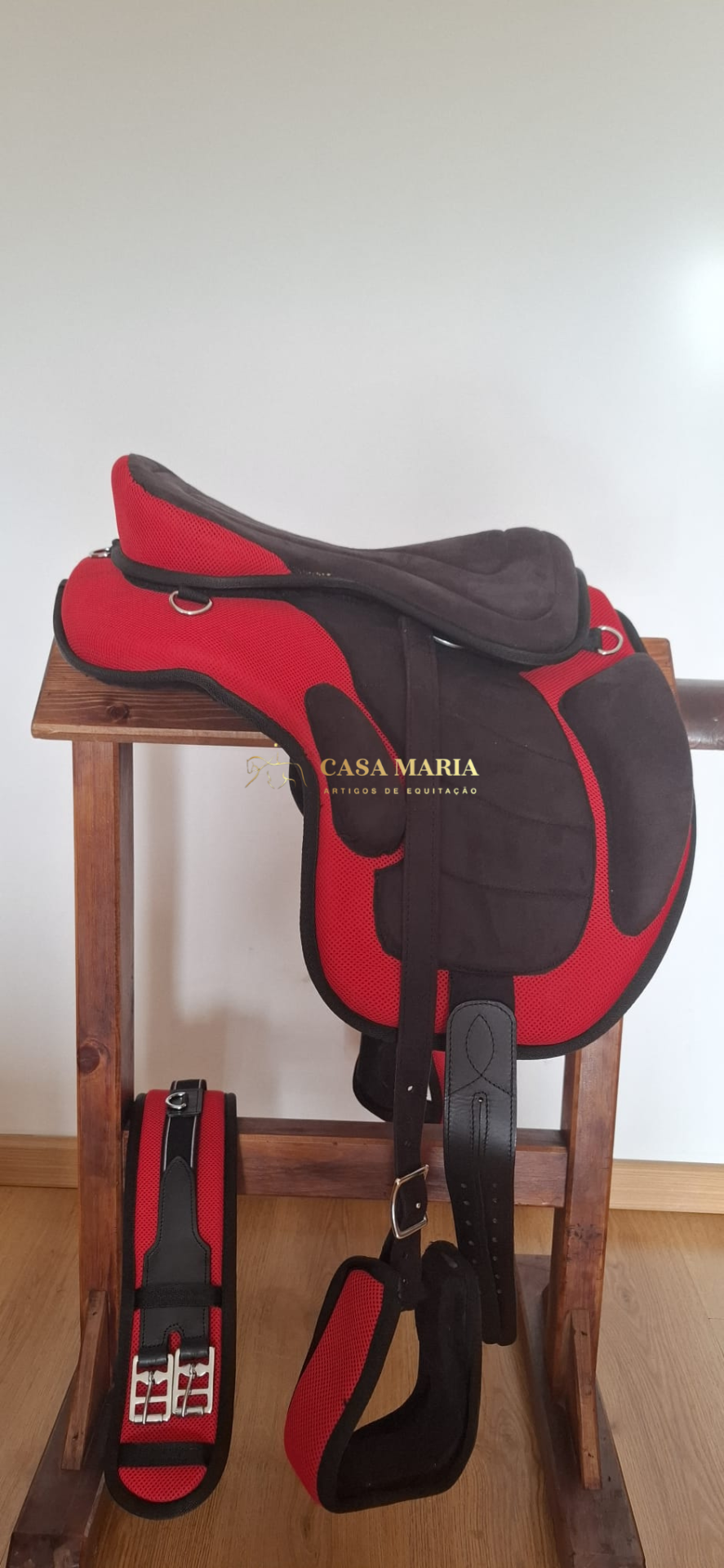 Sela de equitação vermelha e preta com correia preta sobre suporte de madeira