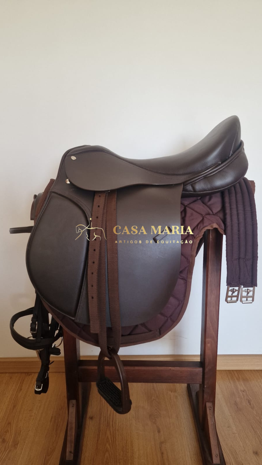 Sela de equitação castanha escura sobre almofada castanha em suporte de madeira