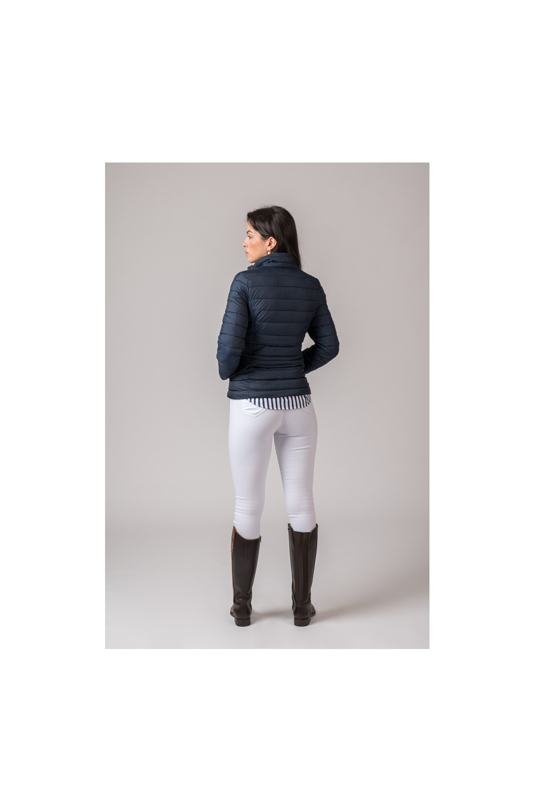 Mulher vista de costas com casaco azul escuro acolchoado, calças brancas e botas castanhas.