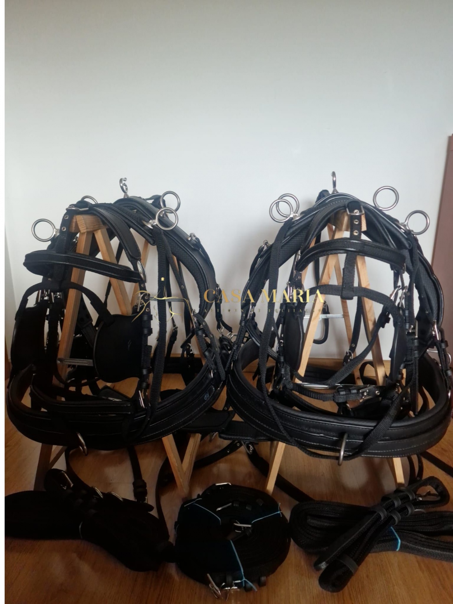Arreios de cavalo pretos em couro com fivelas metálicas prateadas sobre suportes de madeira