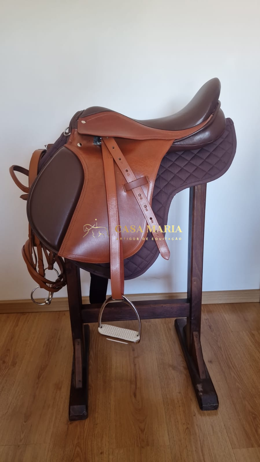 Sela de equitação em pele castanha sobre almofada matelassada castanha numa estrutura de madeira.