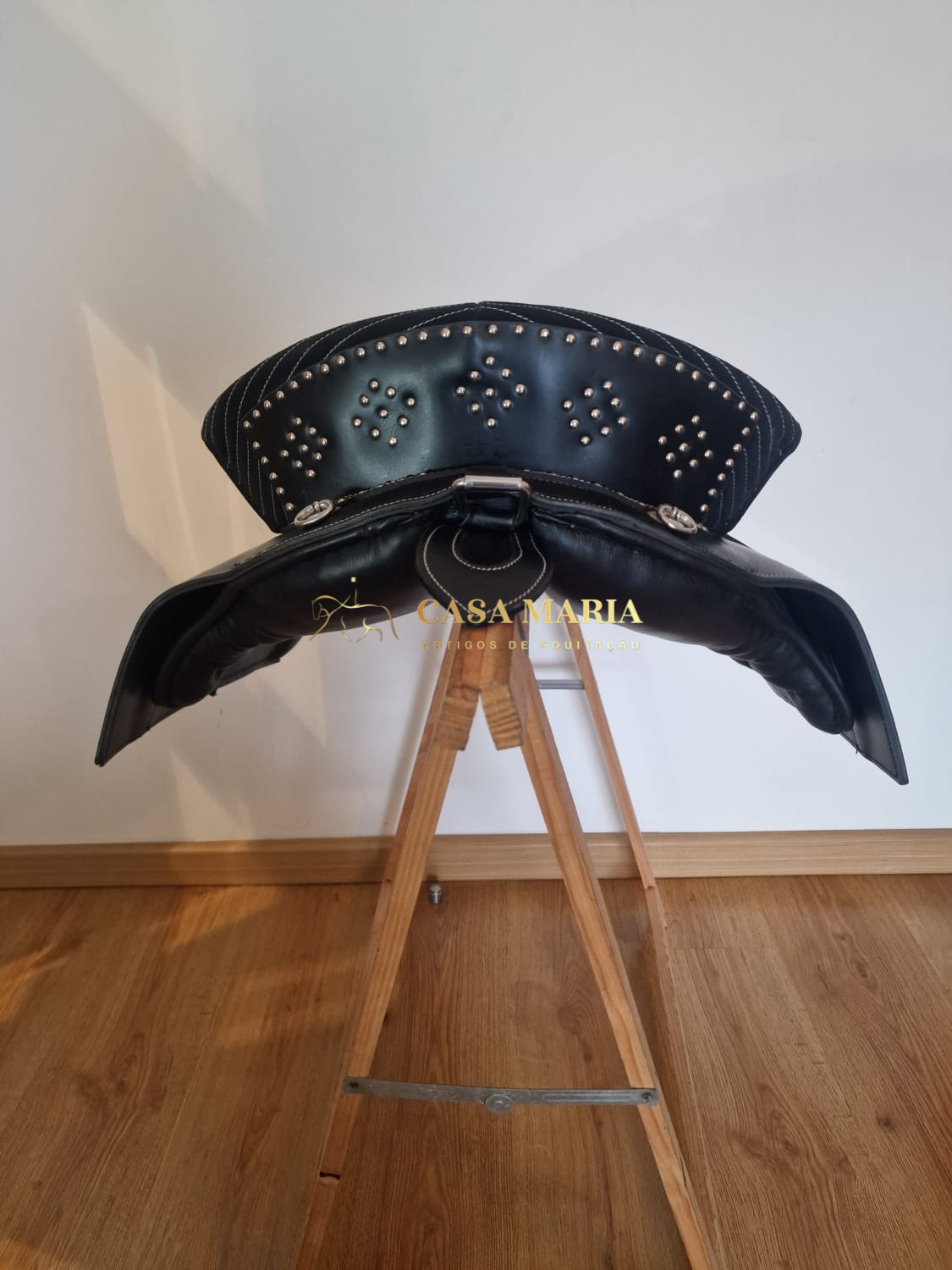 Sela de couro preta com tachas metálicas e suporte de madeira