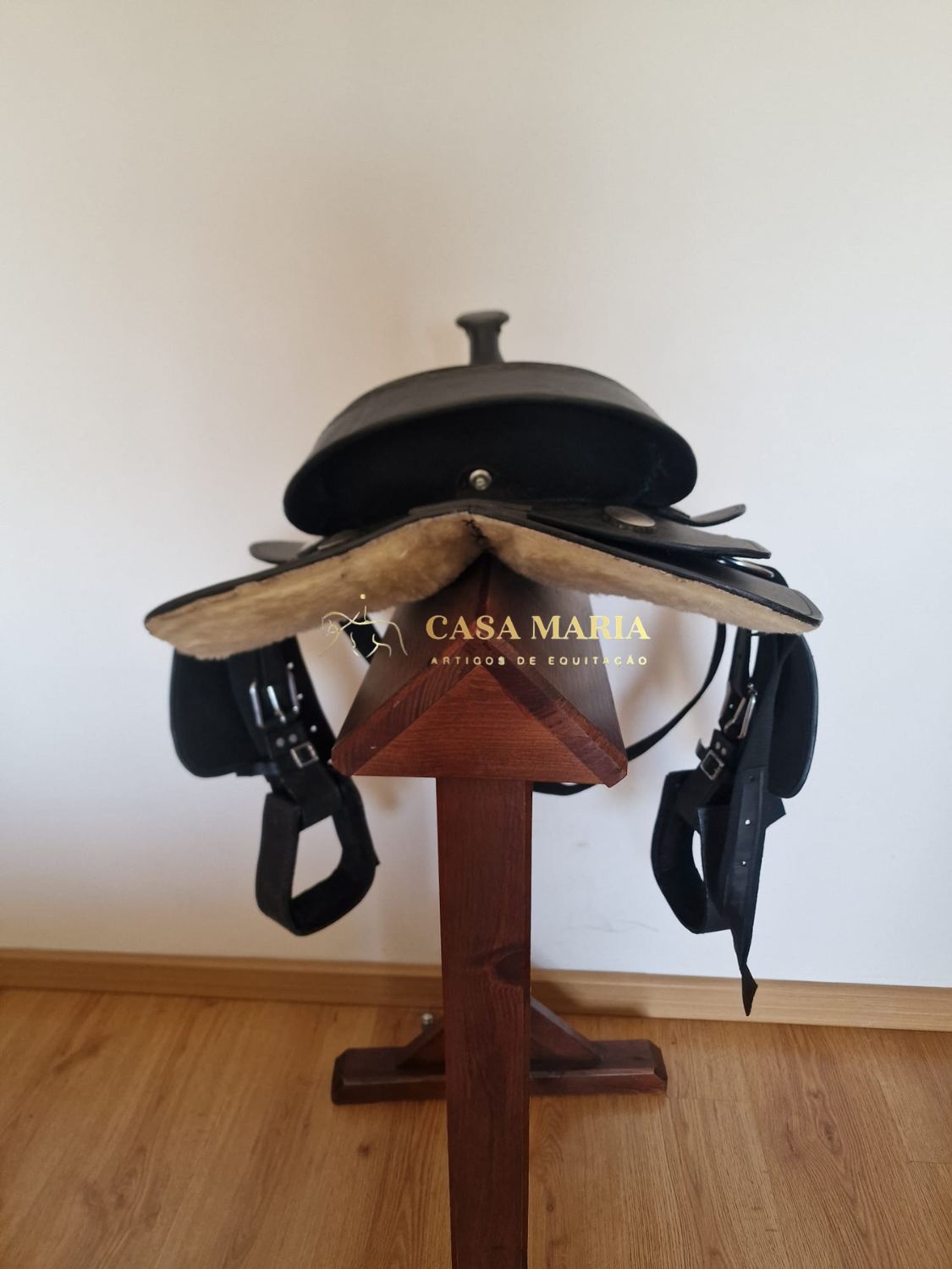 Sela de equitação preta em couro com interior almofadado bege em suporte de madeira.