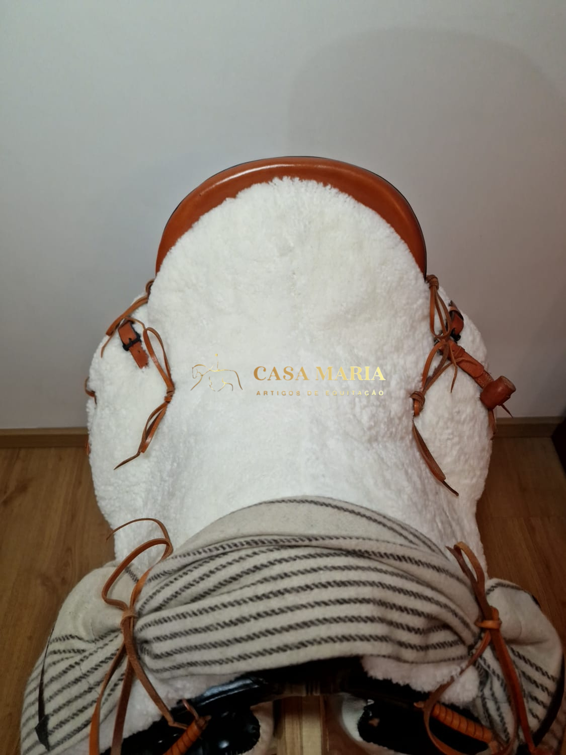 Sela de equitação castanha com almofada branca felpuda e manta riscada cinza-bege