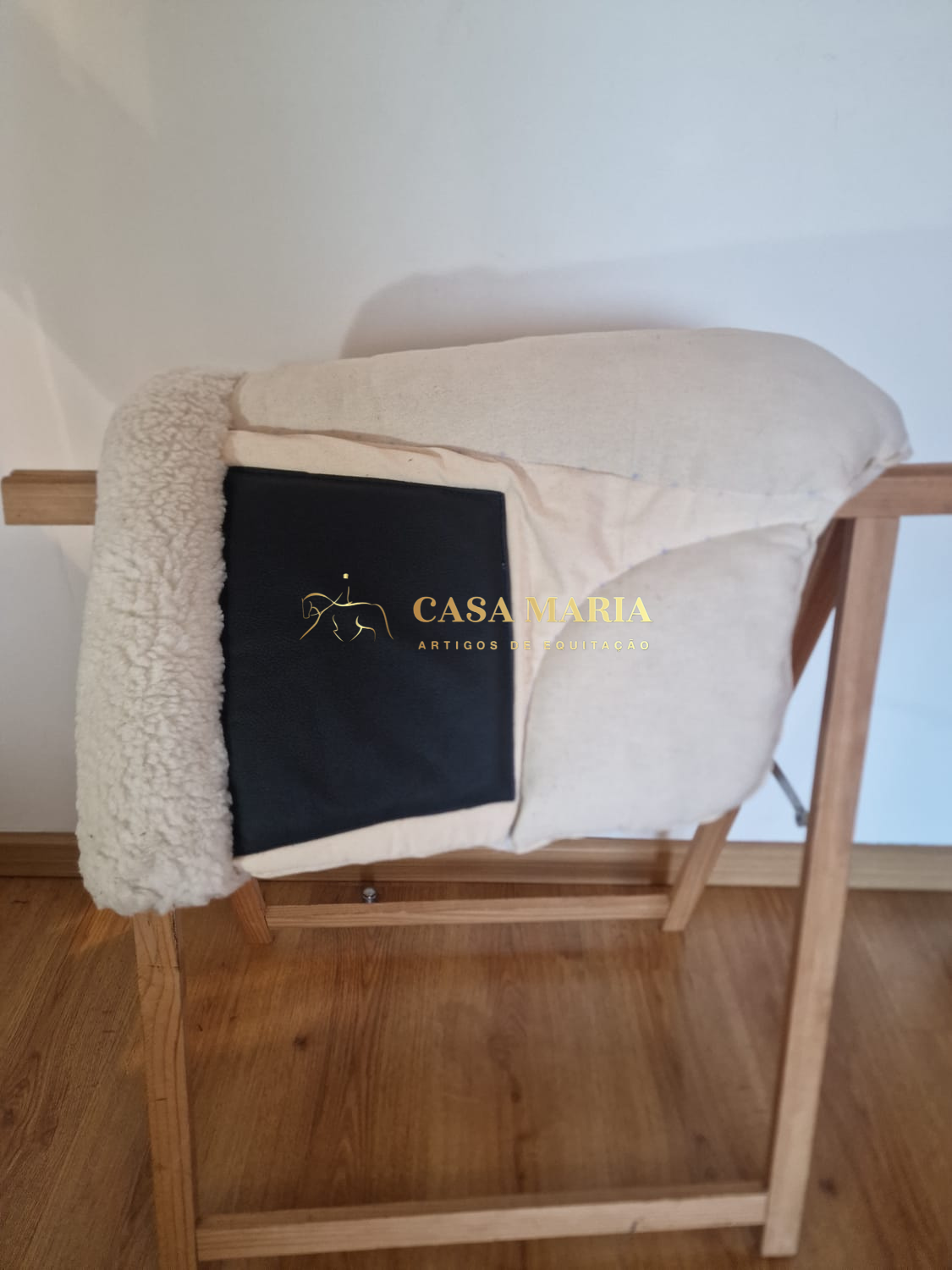 Sela de equitação bege e preta numa estrutura de madeira