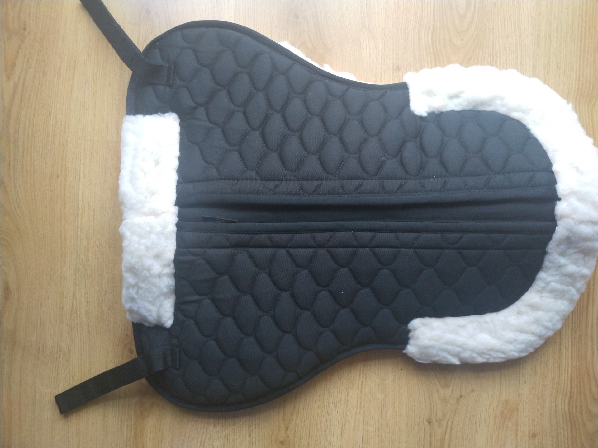 Suporte para sela de cavalo acolchoado preto com bordas brancas felpudas sobre madeira clara