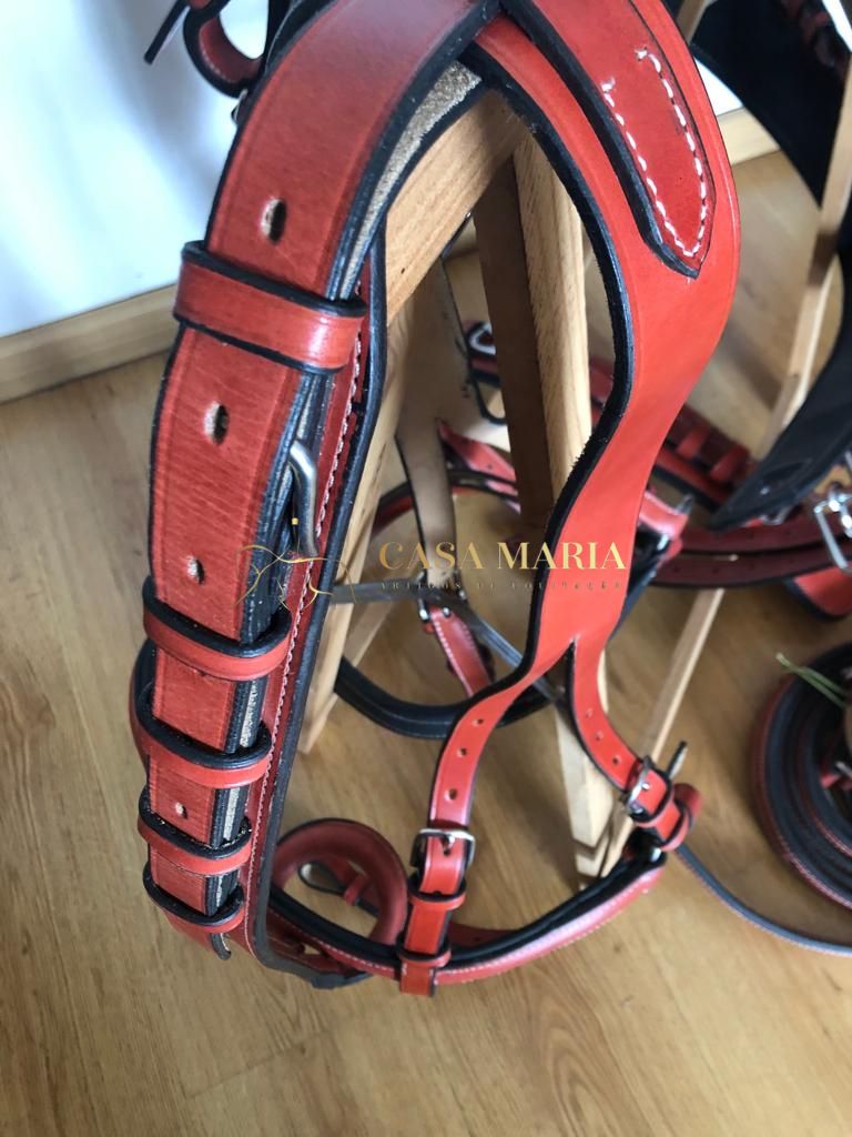 Sela de couro laranja com fivelas metálicas pendurada em suporte de madeira