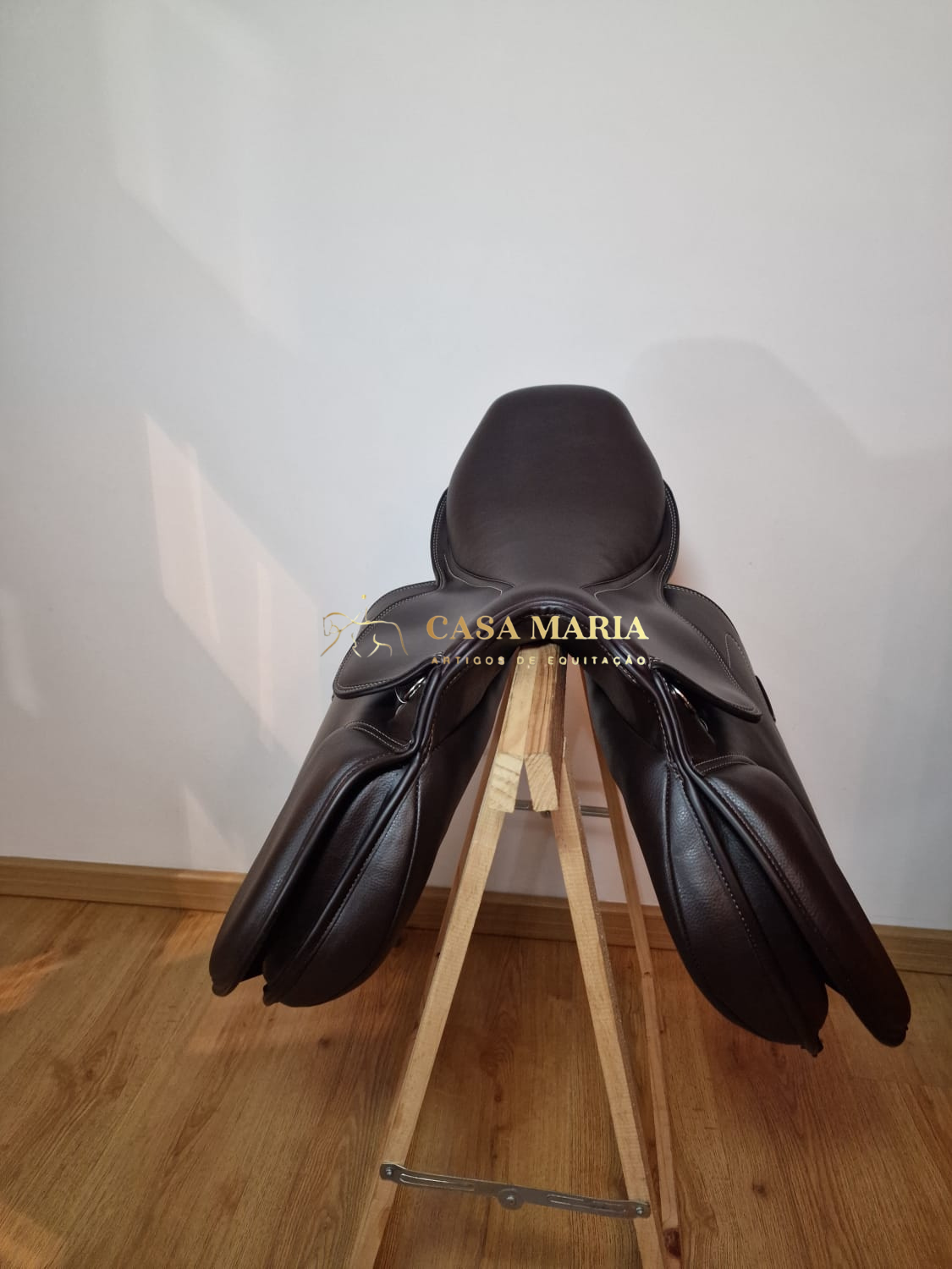 Sela de equitação castanha escura em suporte de madeira