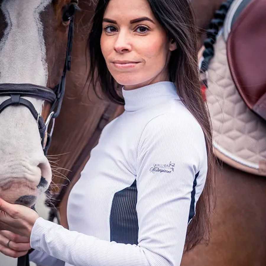 Mulher com blusa branca de manga comprida junto a cavalo castanho e branco