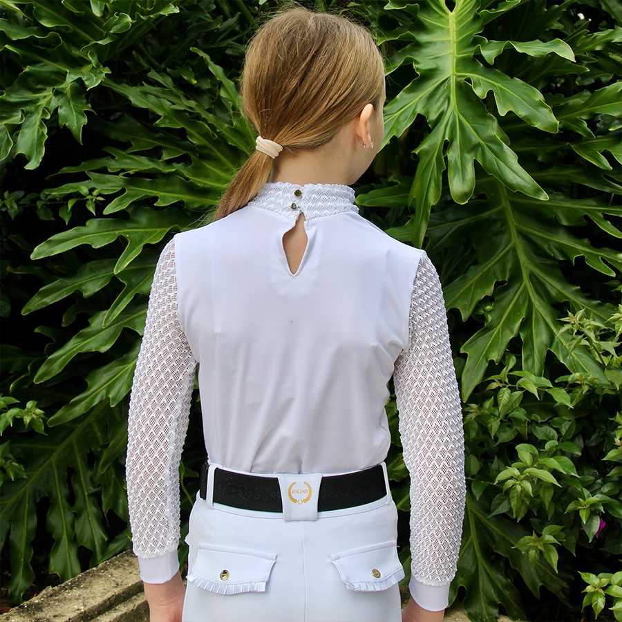 Pessoa de costas com camisa branca rendada e calças brancas com cinto preto, em fundo de folhas verdes