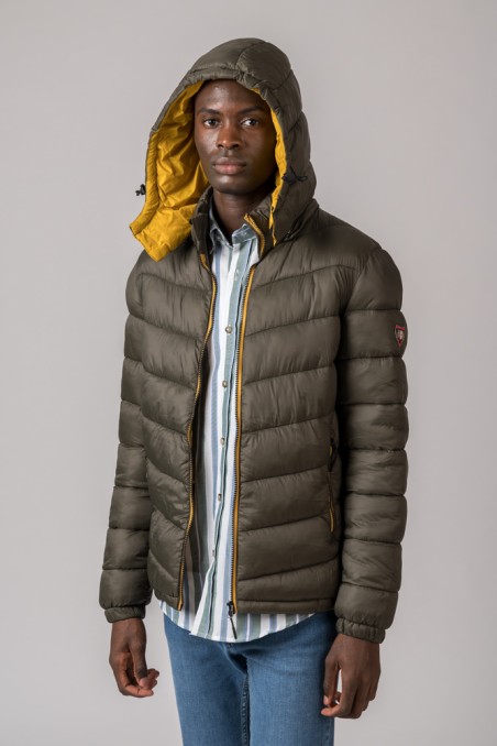 Homem com casaco acolchoado verde-oliva com interior amarelo e capuz, camisa riscada e jeans azuis