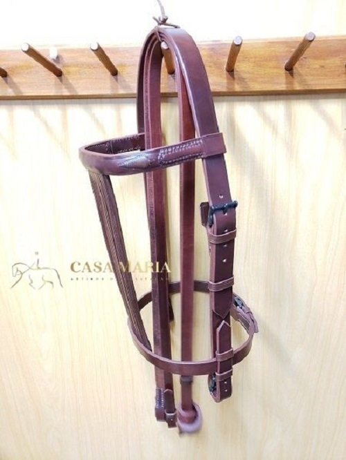 Bridão de pele marrom pendurado em cabide de madeira com logo CASA MARIA