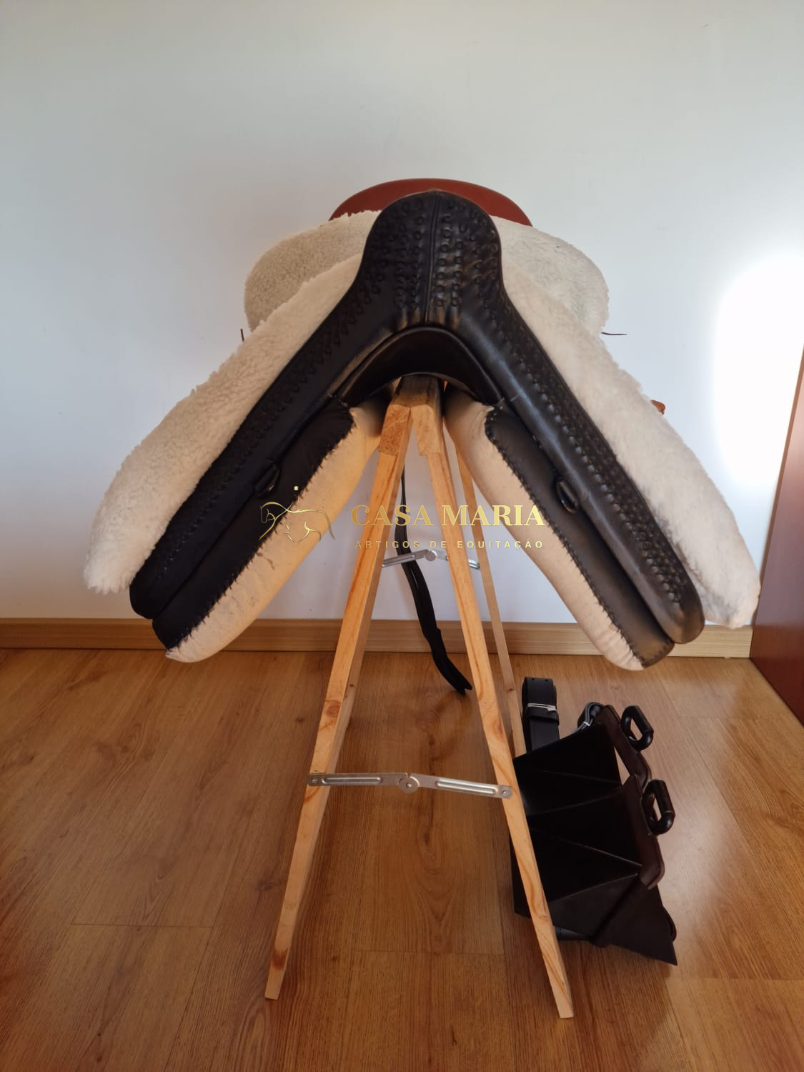 Sela de equitação castanha e preta com revestimento branco em suporte de madeira