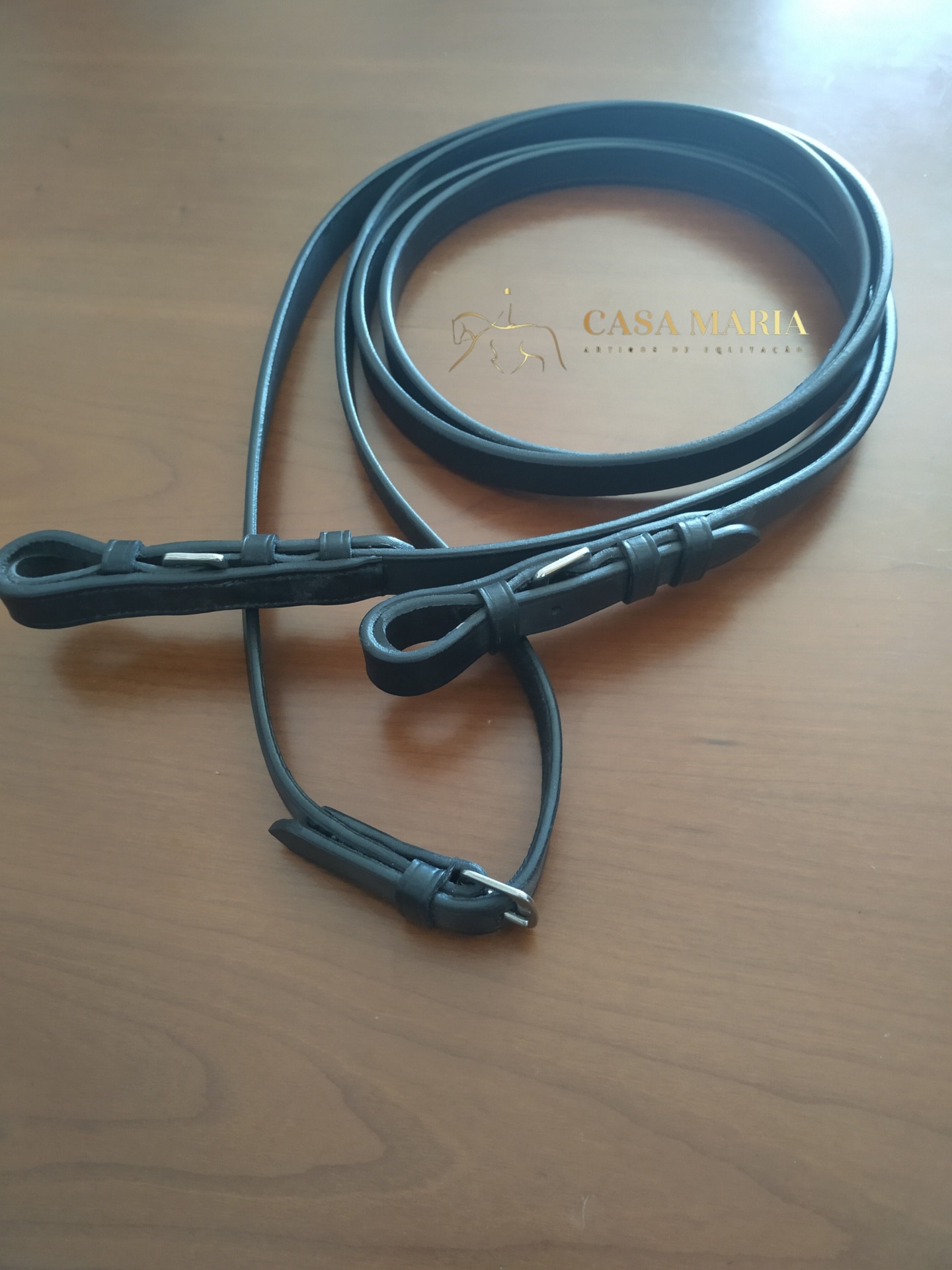 Rédea preta em couro com fivelas metálicas sobre mesa de madeira clara