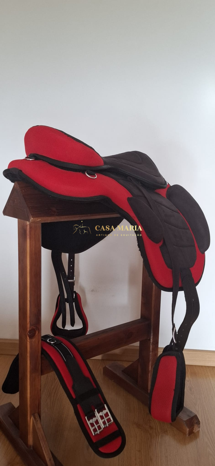 Sela de equitação vermelha e preta num suporte de madeira