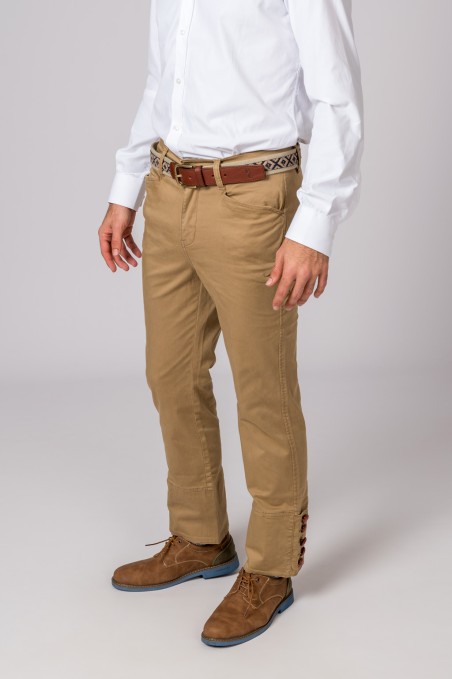 Homem vestido com pantalonas bege, camisa branca, cinto castanho com padrão e sapatos castanhos.