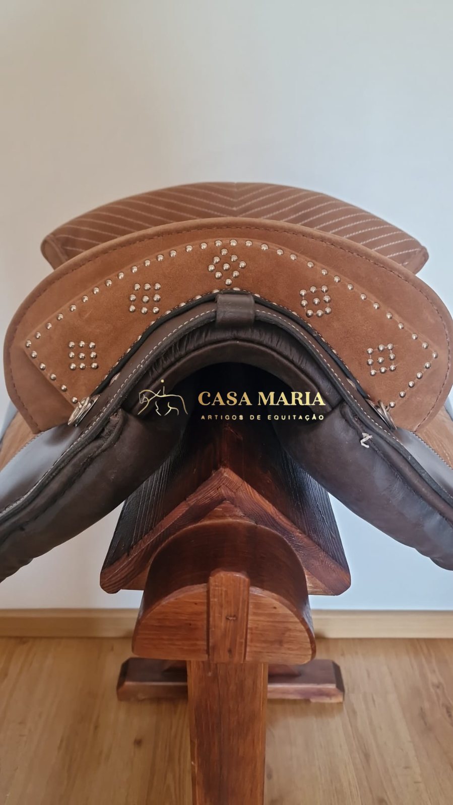 Sela de equitação em camurça castanha e couro preto sobre suporte de madeira