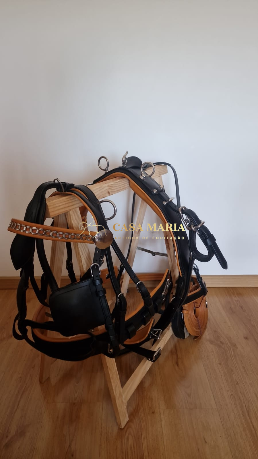 Arnês equino em couro preto e castanho com elementos metálicos em suporte de madeira