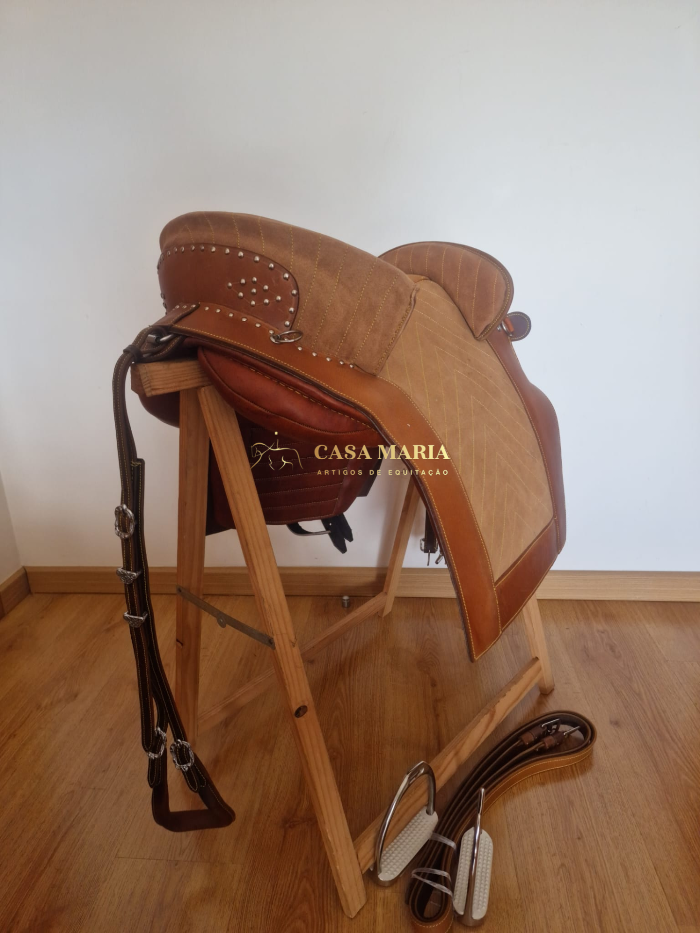 Sela de equitação castanha em suporte de madeira num chão de madeira clara