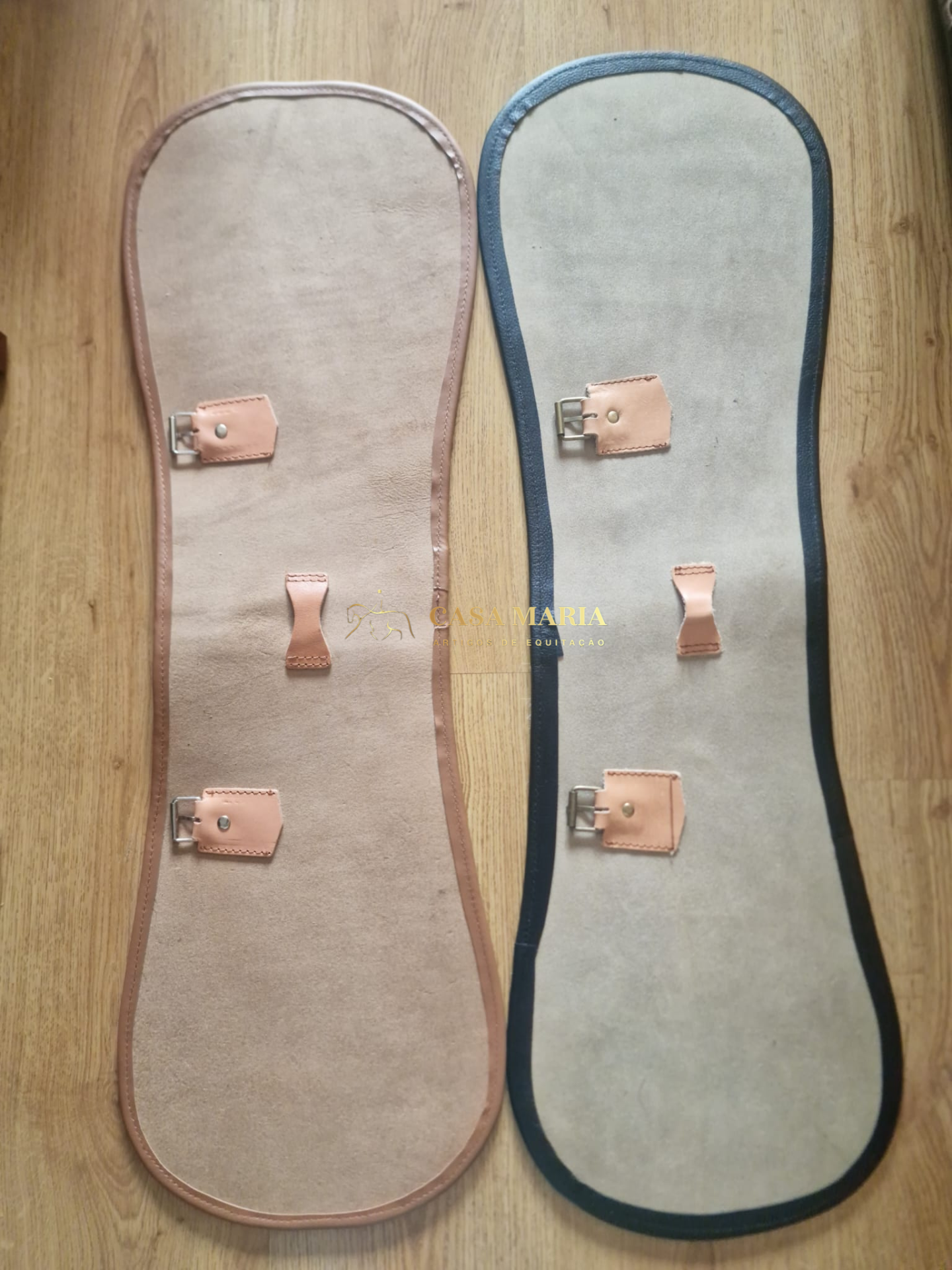 Protetores de estribos em camurça bege com detalhes em castanho e azul escuro sobre chão de madeira