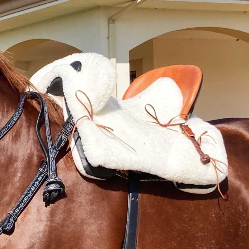 Sela de cavalo com revestimento branco felpudo e assento castanho claro em cavalo castanho