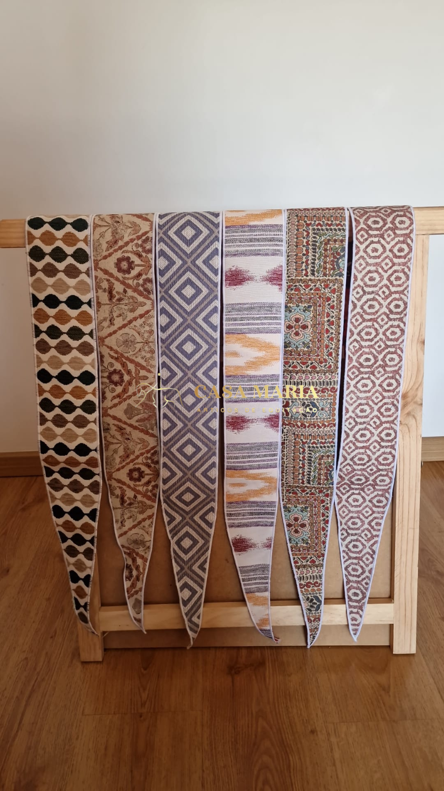 Seis fitas têxteis coloridas com padrões variados penduradas em suporte de madeira