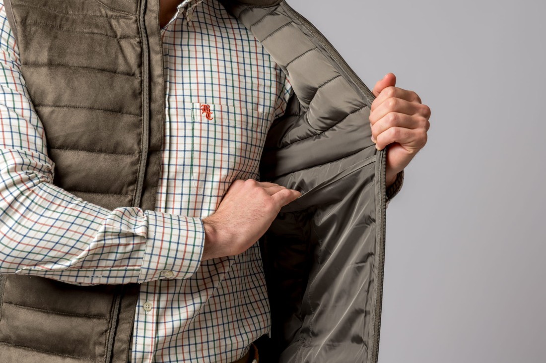 Homem a usar camisa às riscas e colete verde militar acolchoado com interior cinzento acetinado