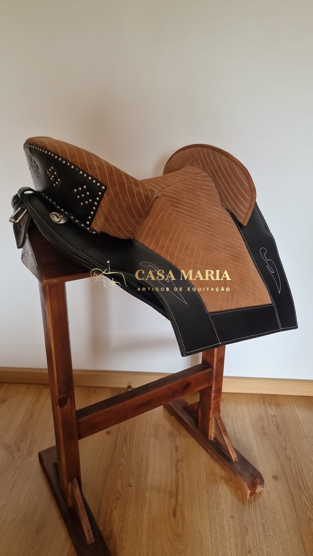 Sela de equitação bege e preta sobre suporte de madeira