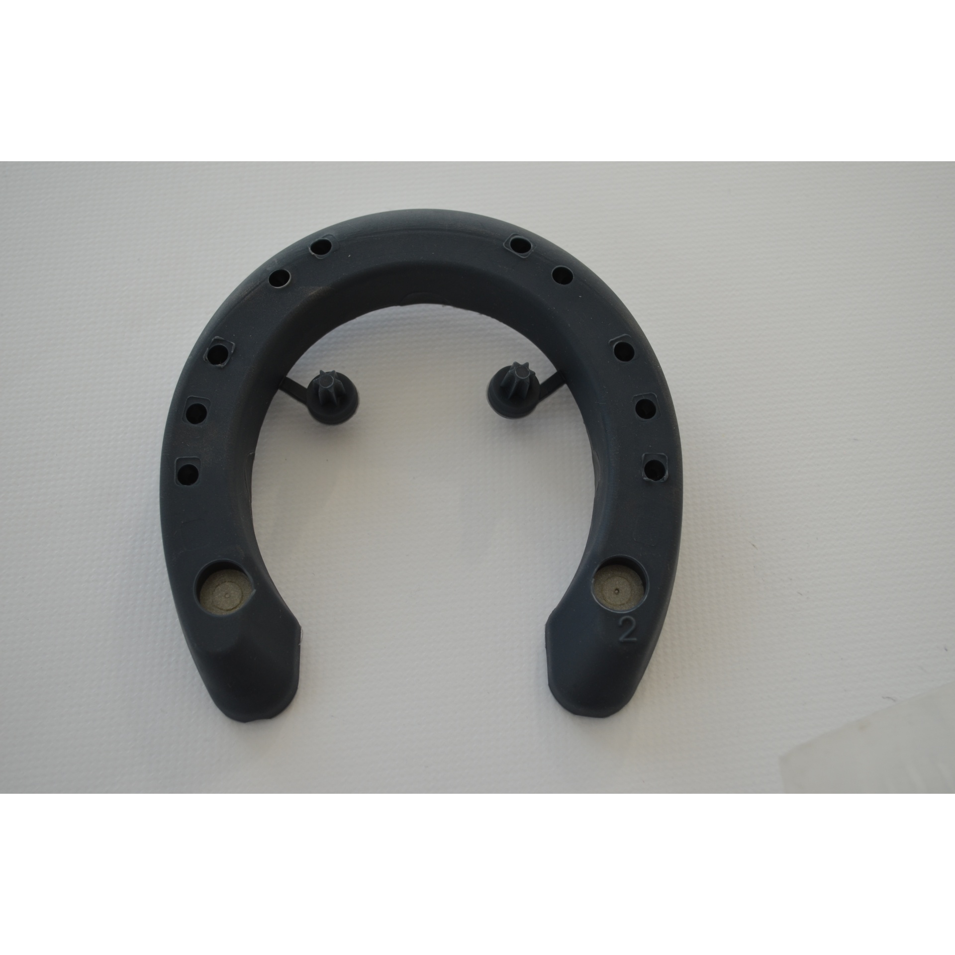 Peça preta em formato de ferradura com furos e pinos sobre fundo branco