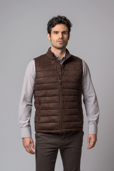Homem com colete castanho acolchoado e camisa de riscas em fundo cinzento