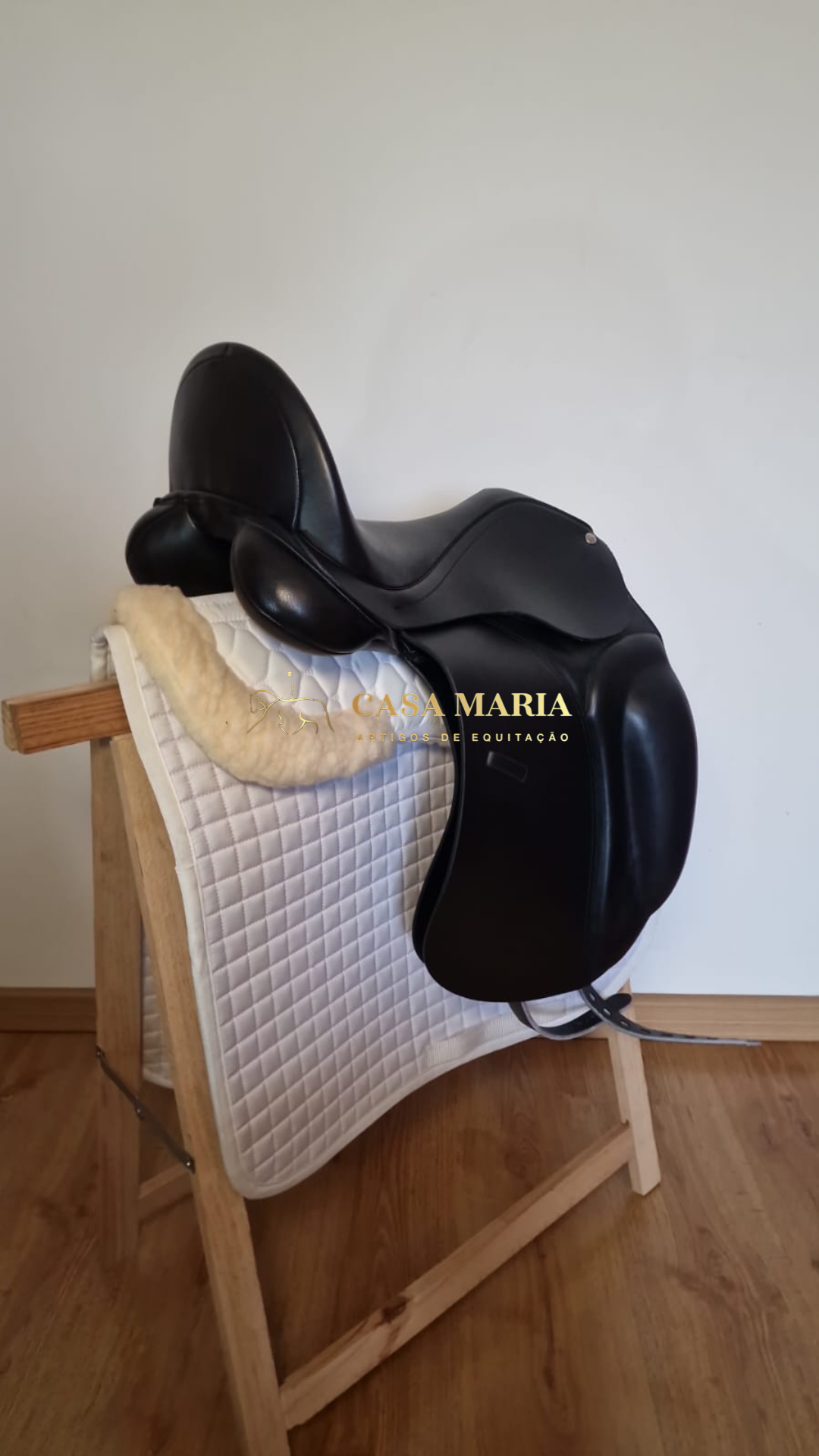 Sela de equitação preta sobre almofada branca acolchoada num suporte de madeira