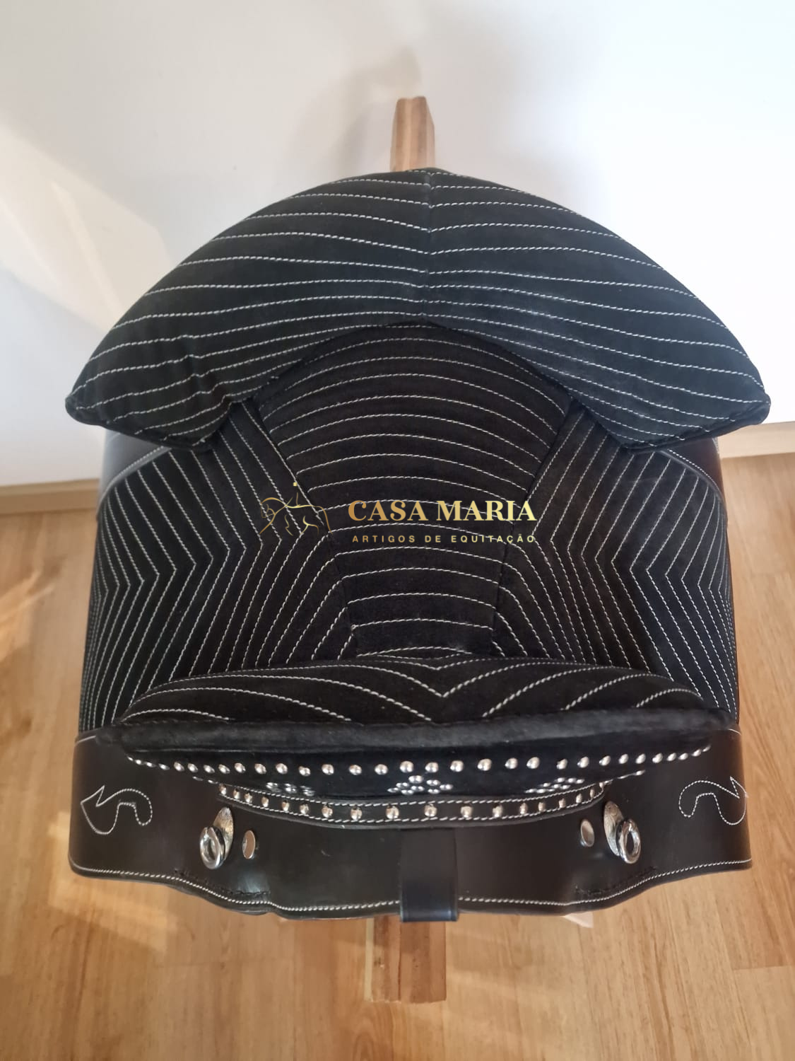 Sela de equitação preta com costuras e tachas metálicas, com inscrição CASA MARIA ARTIGOS DE EQUITAÇÃO