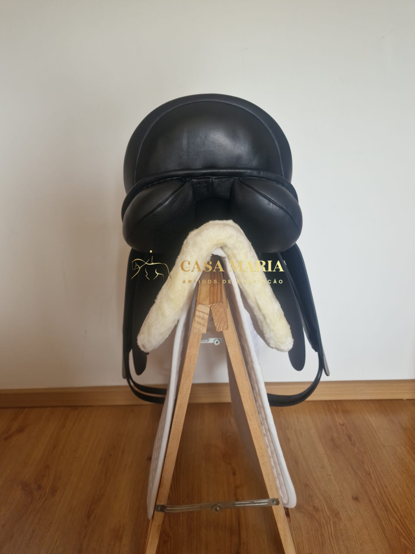 Selim de equitação preto com acolchoamento branco sobre estrutura de madeira