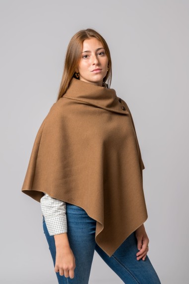 Capa castanha tipo poncho com botões no ombro, usada por modelo com camisa branca e jeans azuis