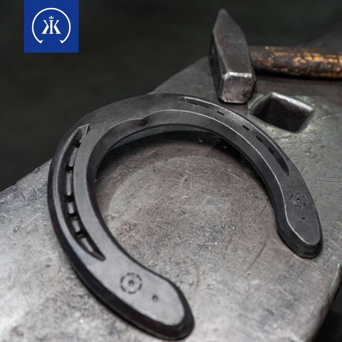 Ferradura preta sobre bigorna cinza com martelo antigo ao fundo