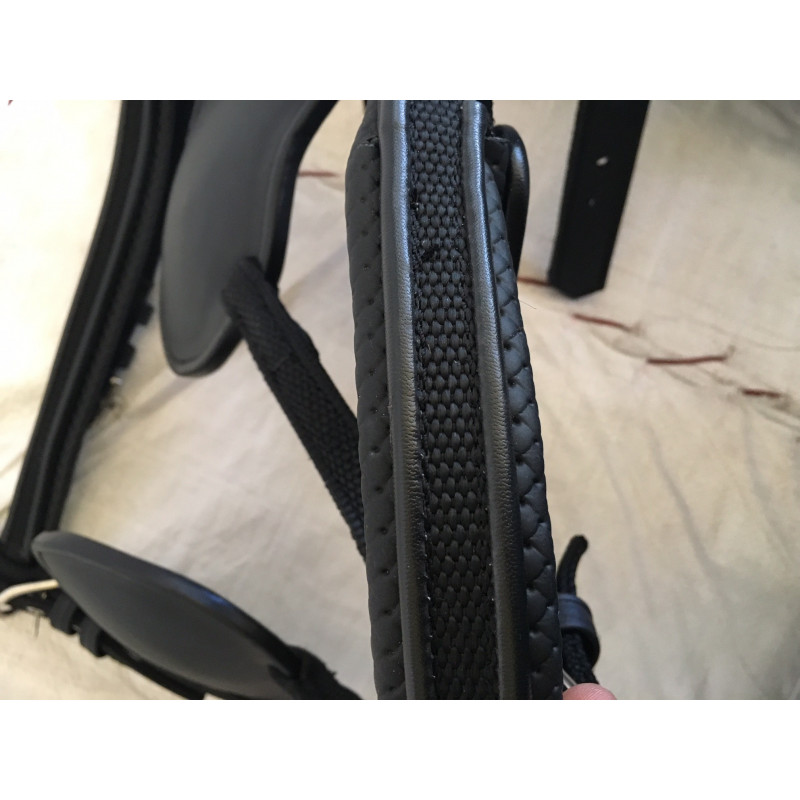 Parte de equipamento em pele preta com textura e fibras entrelaçadas sobre fundo bege