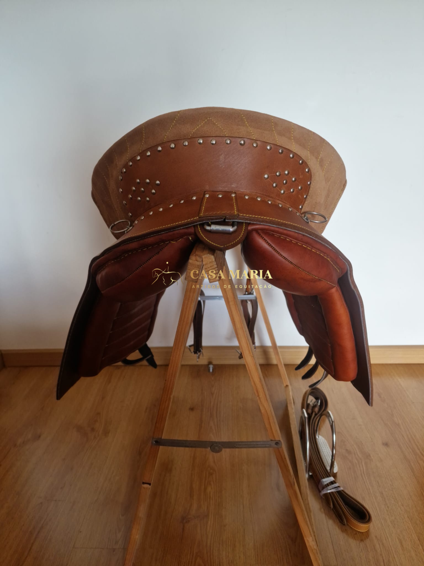 Sela de equitação castanha em suporte de madeira com rêmens ao lado