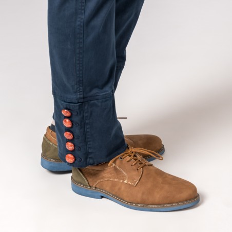 Calças azuis com botões vermelhos e sapatos castanhos com sola azul num fundo claro
