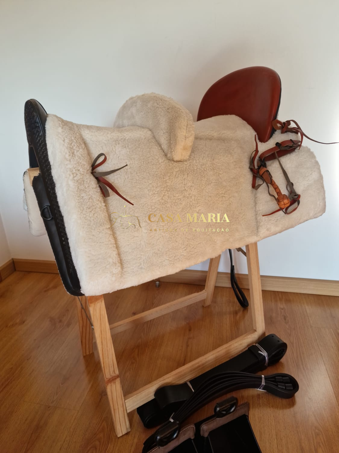Sela de equitação castanha com revestimento branco em suporte de madeira