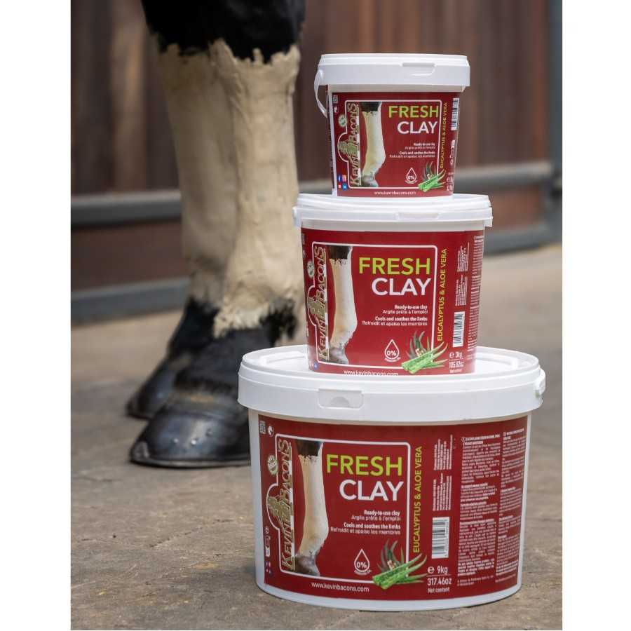 Três baldes de argila Fresh Clay para cuidados com patas de cavalo, empilhados em piso de cimento, com patas de cavalo ao fundo.