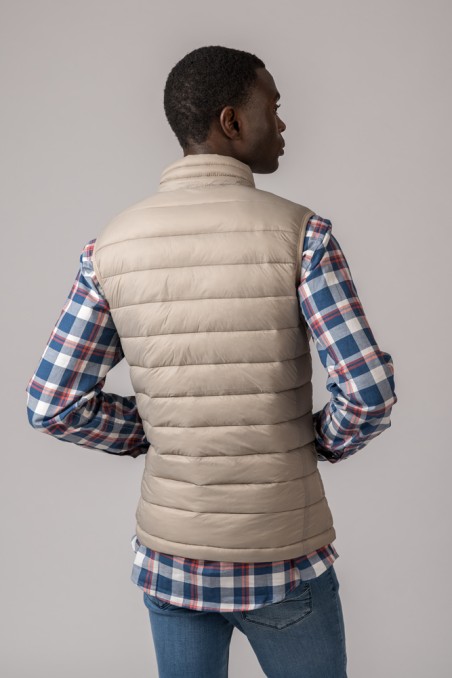 Colete bege acolchoado usado por cima de camisa xadrez azul e branca com calças azuis