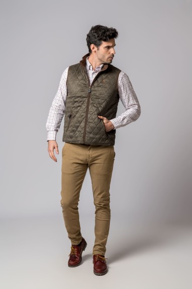 Homem com colete verde acolchoado, camisa xadrez bege e branco, calças bege e sapatos castanhos