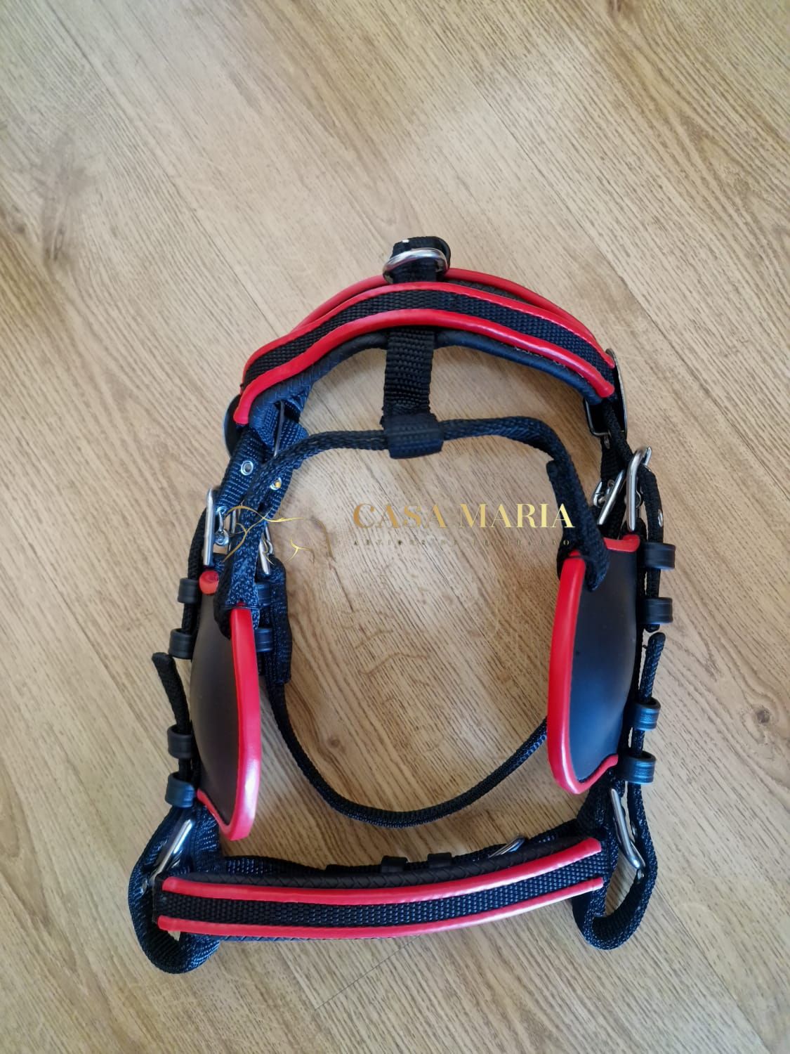 Arnês preto e vermelho para animal de estimação sobre chão de madeira clara