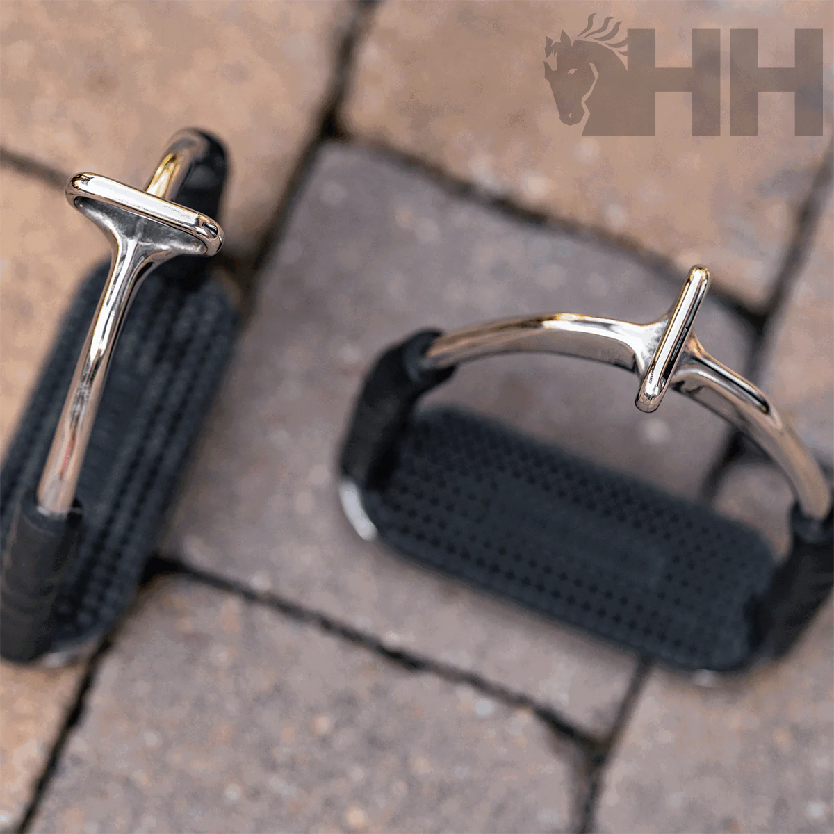 Estribos de equitação metálicos com antiderrapante preto sobre pavimento de pedras