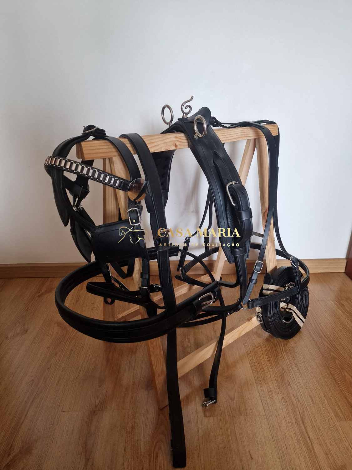 Arreio de couro preto com fivelas metálicas pendurado num cabide de madeira