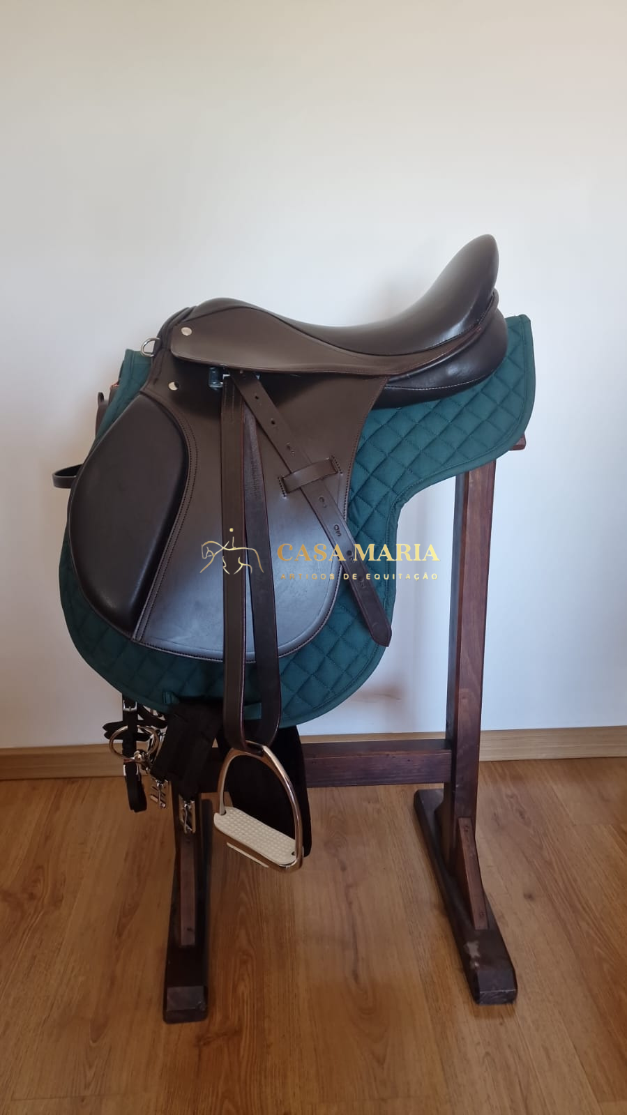 Sela de equitação castanha com alforges e estribos num suporte de madeira