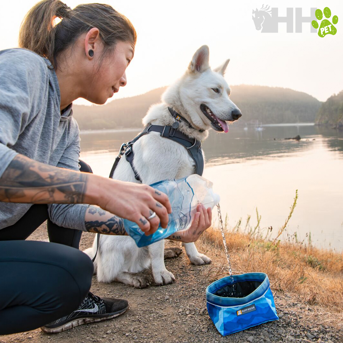Mulher a dar água a um cão com bebedouro portátil junto a um lago ao pôr do sol