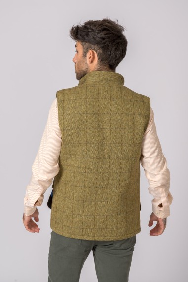 Homem de costas com colete xadrez verde sobre camisa bege listrada e calças verdes